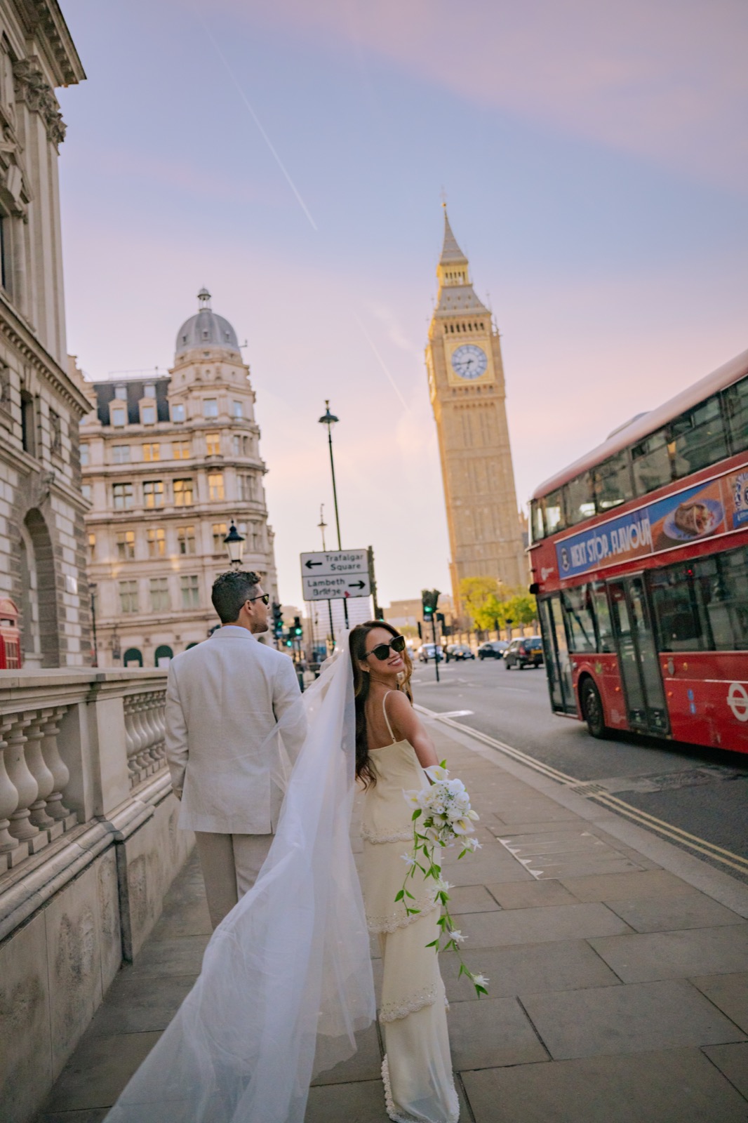 Rachel and Gustavo walking past Big Ben as a red London bus passes